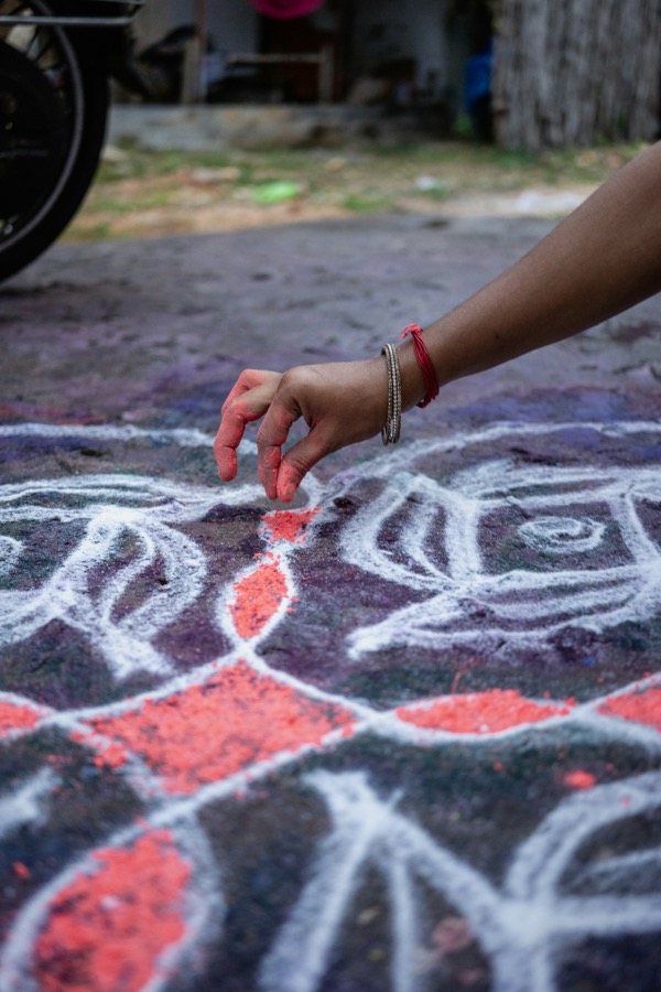A hand drawing a kolam in white rice flour at a doorstep