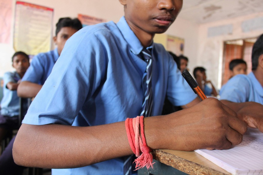 A student in a striped school tie writing in his notebook at a wooden desk